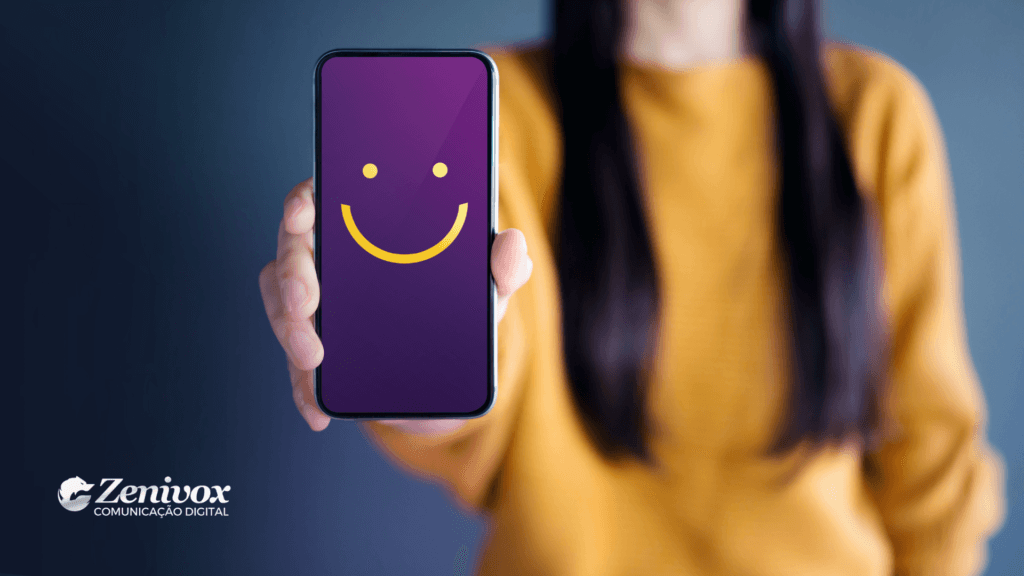 Imagem de uma pessoa segurando um smartphone com a tela exibindo um rosto sorridente em roxo e amarelo. O fundo desfocado destaca a figura central, que veste uma blusa amarela, simbolizando positividade e a centralidade do cliente. O logo da Zenivox Comunicação Digital está posicionada no canto inferior esquerdo, reforçando o compromisso com a experiência do cliente.