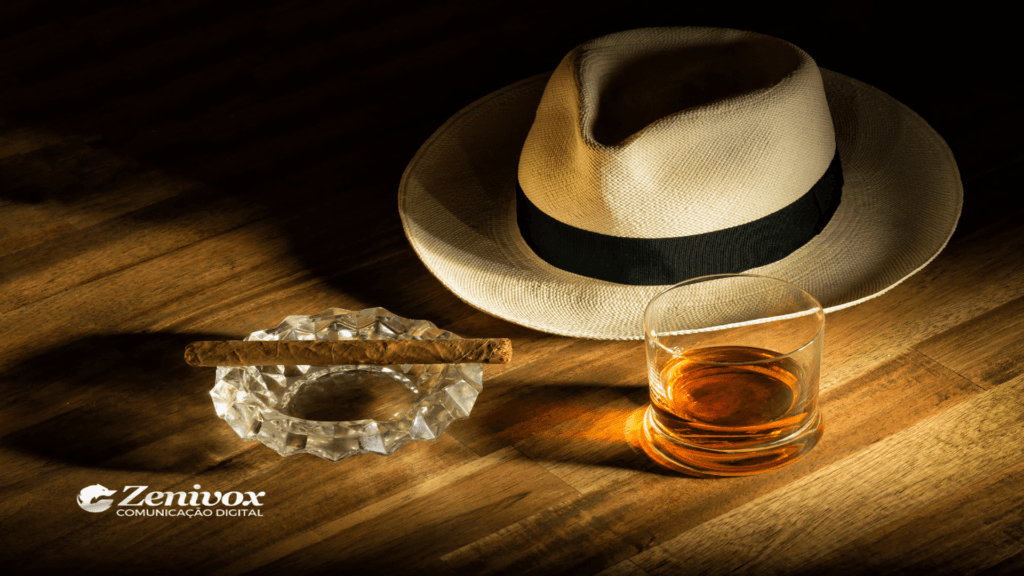 Imagem de um chapéu de palha com faixa preta, acompanhado de um charuto descansando em um cinzeiro de cristal e um copo de rum sobre uma mesa de madeira. Simbolizando a estratégia de branding da Barcadi. O logotipo da Zenivox Comunicação Digital está posicionado no canto inferior esquerdo, representando sofisticação e elegância.