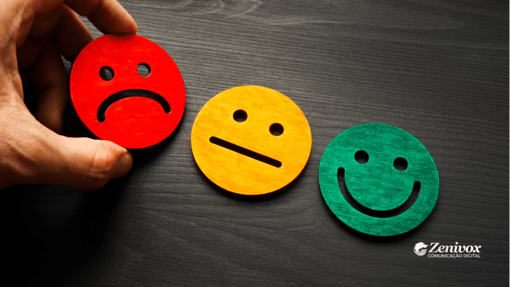 Imagem de três rostos em cores diferentes representando emoções: um rosto triste em vermelho, um neutro em amarelo e um sorridente em verde, simbolizando como pedir avaliações para clientes. Um detalhe adicional é uma mão movendo o rosto vermelho, apontando uma mudança de perspectiva.