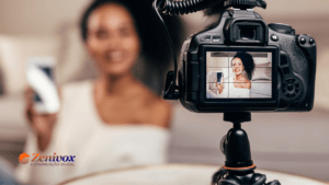 Mulher gravando um vídeo com uma câmera DSLR em um ambiente aconchegante. A tela da câmera foca no rosto da influenciadora, que sorri enquanto segura um smartphone, transmitindo profissionalismo e autenticidade. No canto inferior esquerdo, a marca Zenivox destaca a especialização em comunicação digital. A imagem representa o poder do VSL Marketing, enfatizando como vídeos bem produzidos podem converter leads em clientes de forma eficaz.