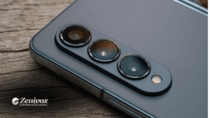 Close-up das câmeras traseiras de um smartphone premium sobre uma superfície de madeira, destacando a qualidade e design do dispositivo, simbolizando o posicionamento de marca da Samsung. No canto inferior esquerdo, o logotipo da Zenivox Comunicação Digital reforça a identidade visual da marca.