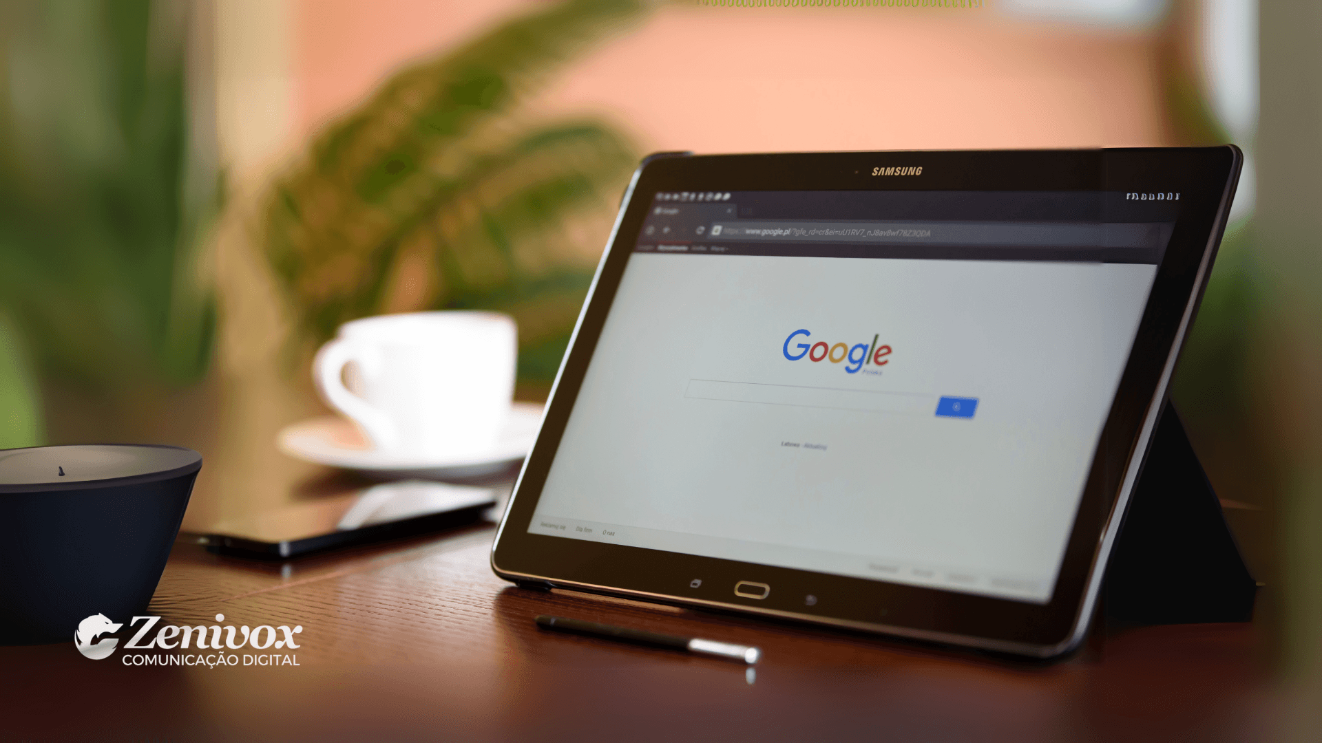 Tablet Samsung exibindo a página inicial do Google, apoiado sobre uma mesa ao lado de um smartphone, uma xícara de café e uma vela decorativa. No canto inferior esquerdo, o logo da Zenivox Comunicação Digital está visível. Imagem representando inovação e desenvolvimento de produtos digitais.