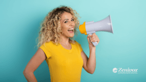 Mulher loira e sorridente segurando um megafone cinza com detalhes amarelos, simbolizando o marketing experiencial. O fundo é azul claro, criando contraste com a camiseta amarela da mulher. No canto inferior direito, o logotipo da Zenivox Comunicação Digital aparece em branco.