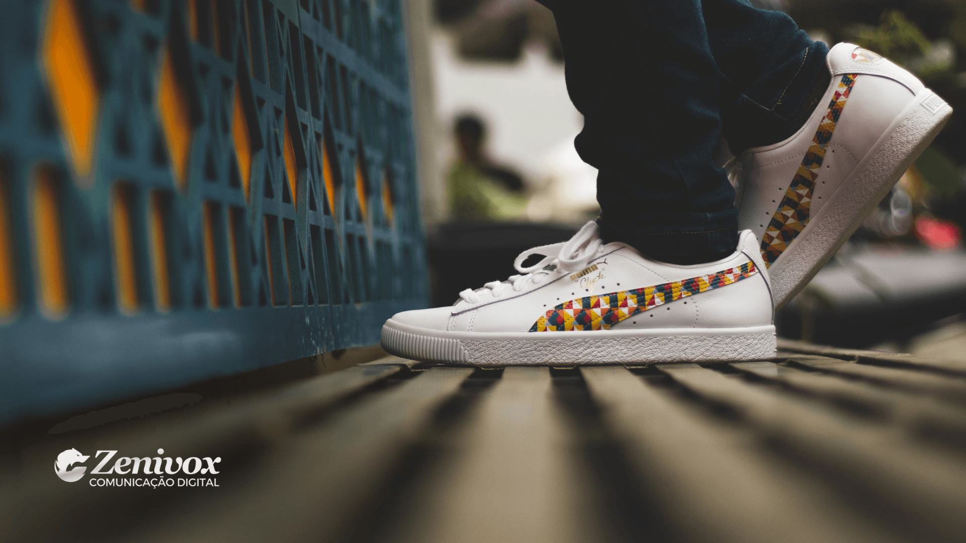 Tênis branco da marca Puma, com detalhes coloridos em forma de mosaico no design lateral, em um ambiente urbano, focado em estilo e atitude. Um elemento visual sonoro que reforça o conceito de velocidade e os 4 Ps do Marketing da Puma.