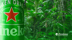 Imagem de uma lata de cerveja Heineken em destaque, com uma floresta tropical verde ao fundo. A lata exibe a icônica estrela vermelha e os detalhes da marca. No canto inferior direito, o logotipo da Zenivox Comunicação Digital está visível. A imagem representa o conceito de Marketing Verde, destacando a conexão entre a Heineken e práticas sustentáveis, simbolizando inovação ecológica e compromisso ambiental.
