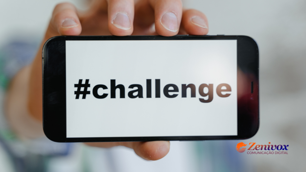 Imagem de uma pessoa segurando um smartphone com a tela exibindo a palavra "#challenge" em letras pretas sobre fundo branco. No canto inferior direito está o logotipo da Zenivox Comunicação Digital.