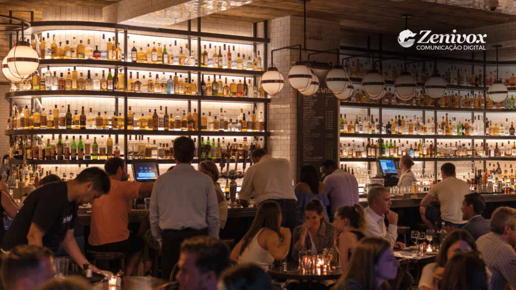 Imagem de um bar sofisticado com uma ampla variedade de bebidas expostas em prateleiras iluminadas, destacando a diversificação e amplitude do portfólio da Pernod Ricard. O ambiente elegante e movimentado transmite a ideia de que a oferta diversificada da marca atende a diferentes públicos e ocasiões. A logomarca da Zenivox está presente no canto superior direito, reforçando a conexão com estratégias de comunicação digital e marketing.