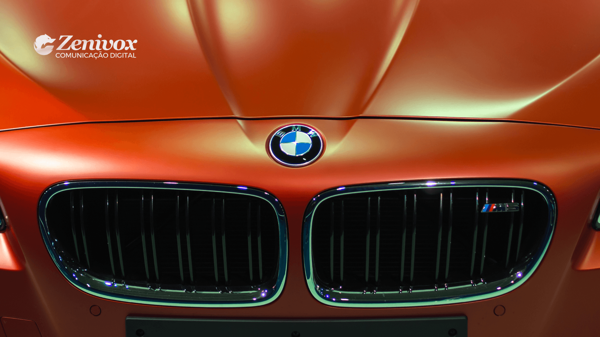 Close-up da grade frontal de uma BMW M5 em cor laranja metálica com o logotipo da Zenivox no canto superior esquerdo, simbolizando sofisticação, exclusividade e excelência na hora de gerar valor ao cliente.