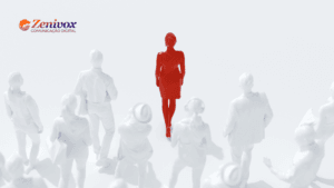 Uma figura feminina em destaque, totalmente vermelha, caminha com confiança entre várias outras figuras brancas, representando a liderança feminina em meio à multidão. No canto superior esquerdo, aparece o logotipo da ZeniVox Comunicação Digital.