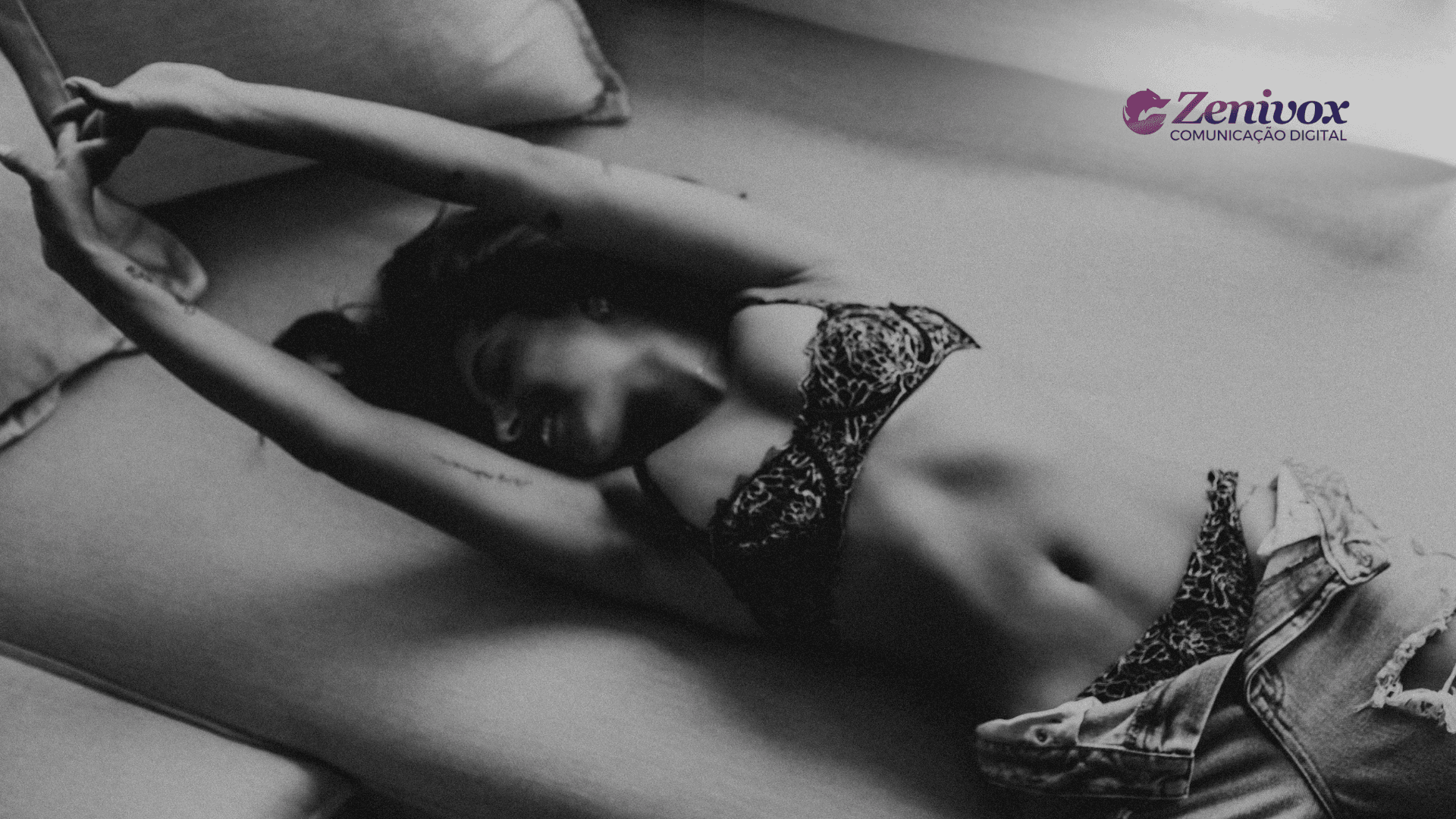 Mulher deitada em um sofá, usando lingerie rendada e jeans, com expressão leve e descontraída. Imagem em preto e branco com tom sensual sutil, transmitindo a ideia de campanhas publicitárias sensuais com elegância sem vulgaridade. Branding da Zenivox visível no canto superior direito.