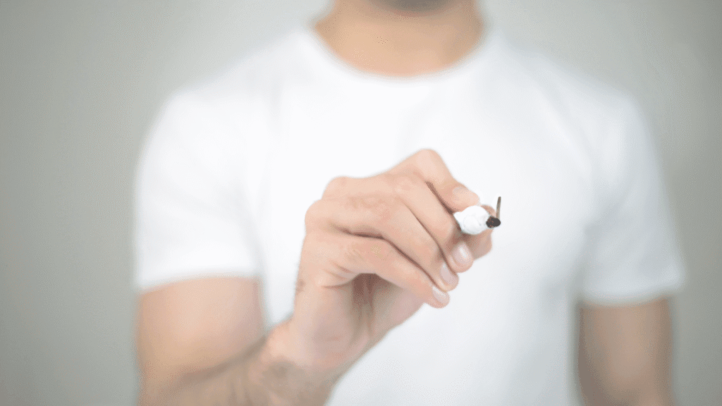 Homem com camiseta branca apontando uma caneta para a câmera, simulando escrita ou desenho em uma tela invisível, representando o início da definição de rebrandings.