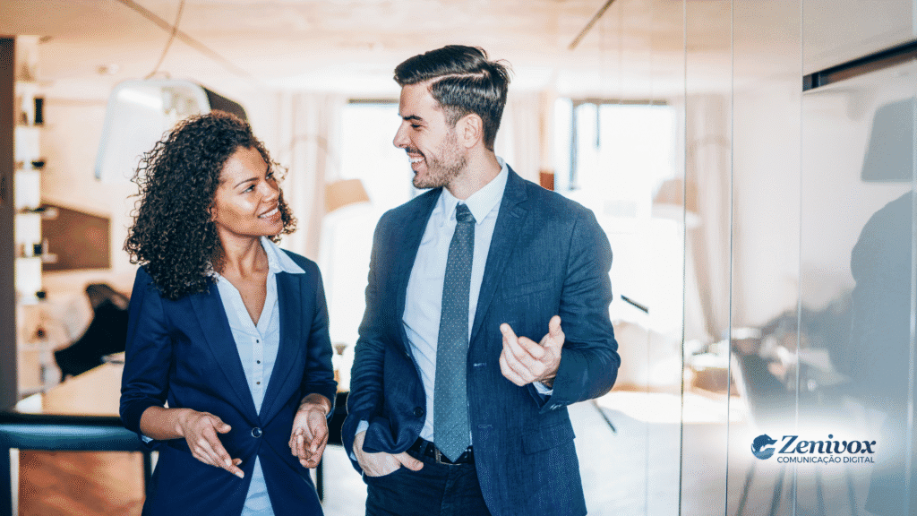 Dois profissionais bem vestidos, sorrindo e conversando de forma leve em um ambiente corporativo, representando uma relação profissional saudável, empática e colaborativa. A cena transmite proximidade, conexão e confiança — elementos fundamentais para um bom relacionamento com o cliente.
