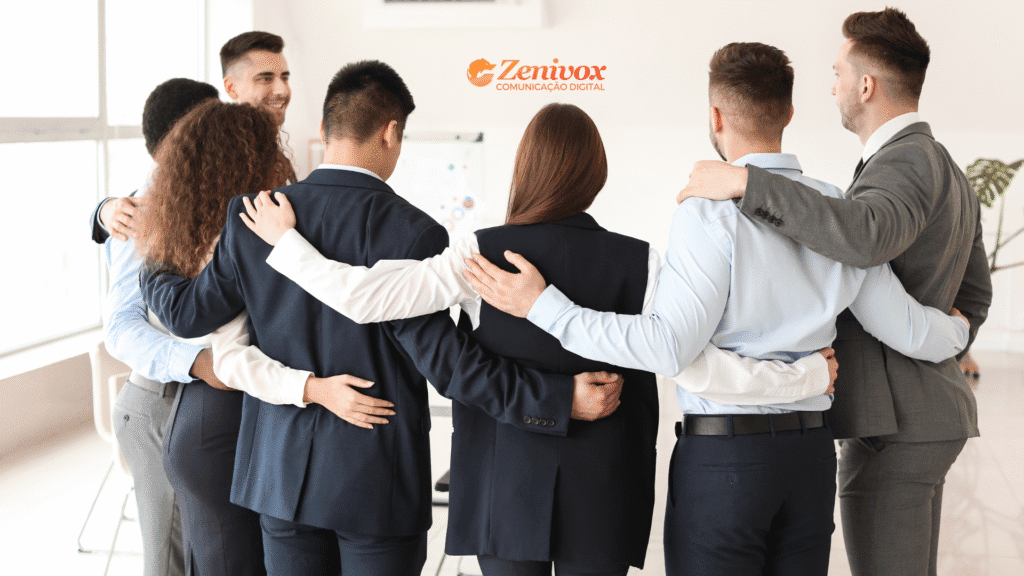 Grupo de profissionais vestidos formalmente, de costas, abraçados em círculo, simbolizando união, empatia e colaboração no ambiente de trabalho. A imagem transmite a ideia de harmonia e fortalecimento dos vínculos após a superação de conflitos pela gestão de conflitos. No topo, o logotipo da Zenivox Comunicação Digital.